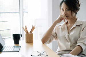 Distracted asian woman dealing with high-functioning anxiety while sitting at her desk at work.