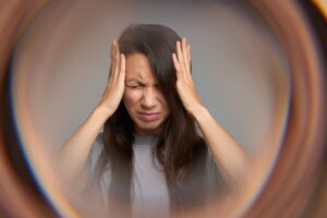 Woman holding her head in distress, illustrating the sensory overwhelm and emotional exhaustion associated with autistic burnout symptoms