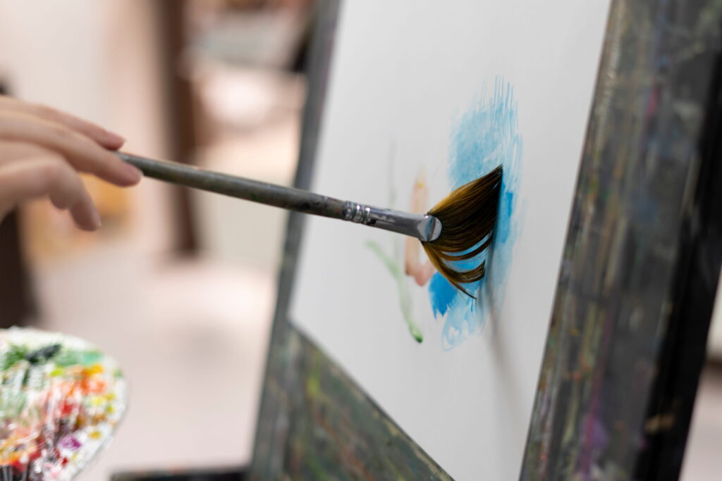 A close-up of a paintbrush applying blue paint to a canvas, illustrating the distinction between art therapy and therapeutic art through the creative process.