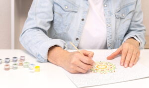 A person painting a mandala using a paint-by-numbers kit, showcasing the benefits of art therapy for relaxation and emotional expression.