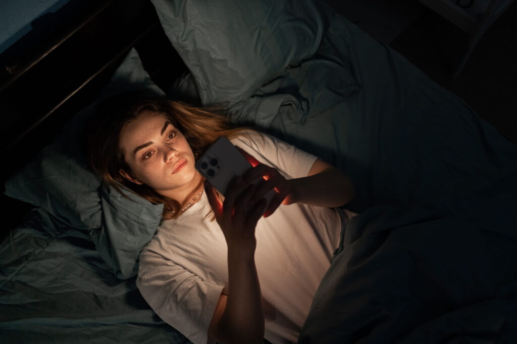 Woman awake at night on her phone reflecting ADHD sleep struggles and overstimulation.