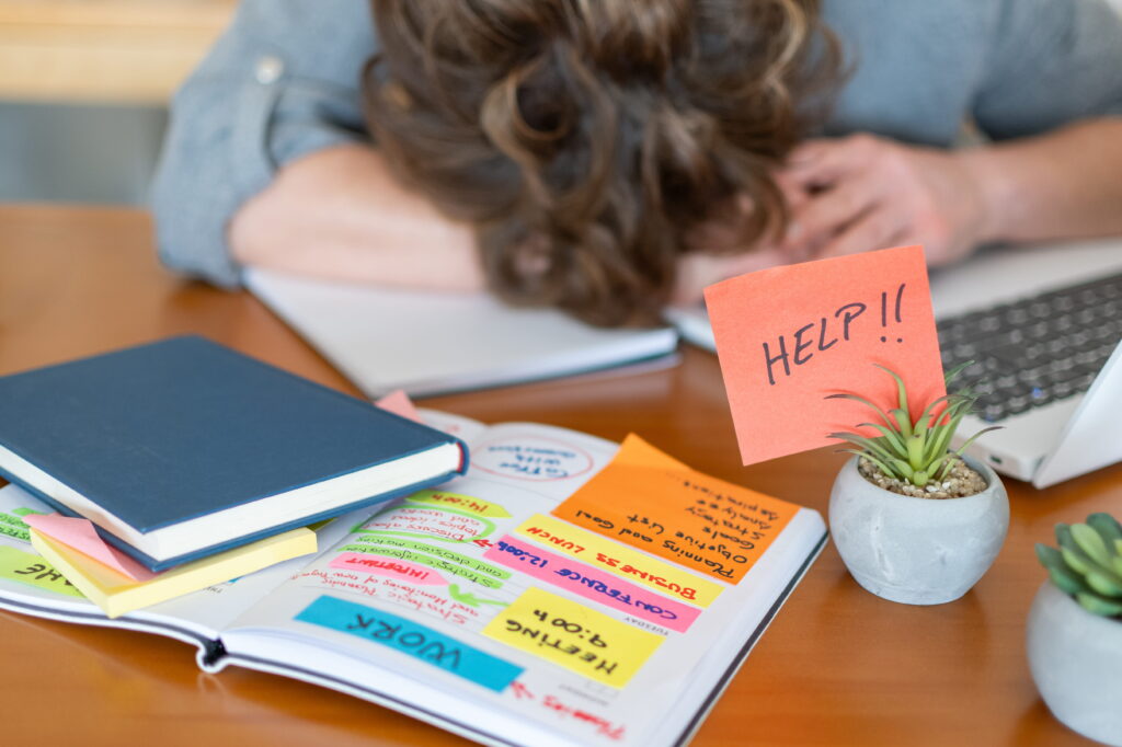 Adult experiencing executive dysfunction in ADHD while sitting overwhelmed at a desk with planner and sticky notes