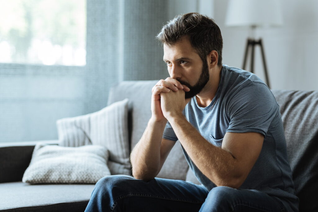 Man sitting on couch looking overwhelmed and emotionally withdrawn at home.