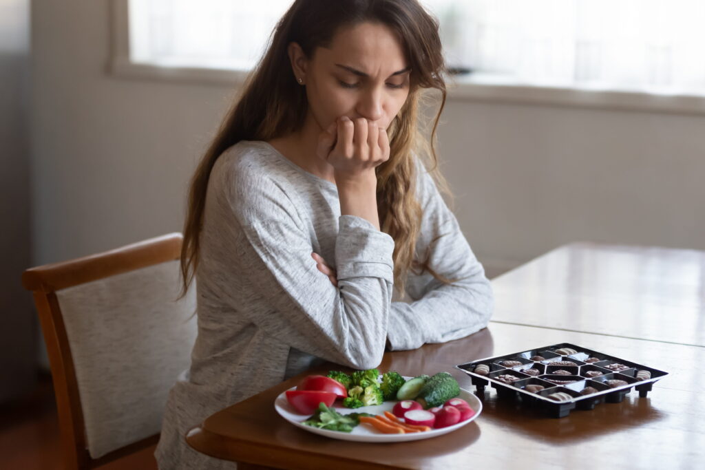Signs of an eating disorder may look like a woman contemplating on candy and a healthy option.